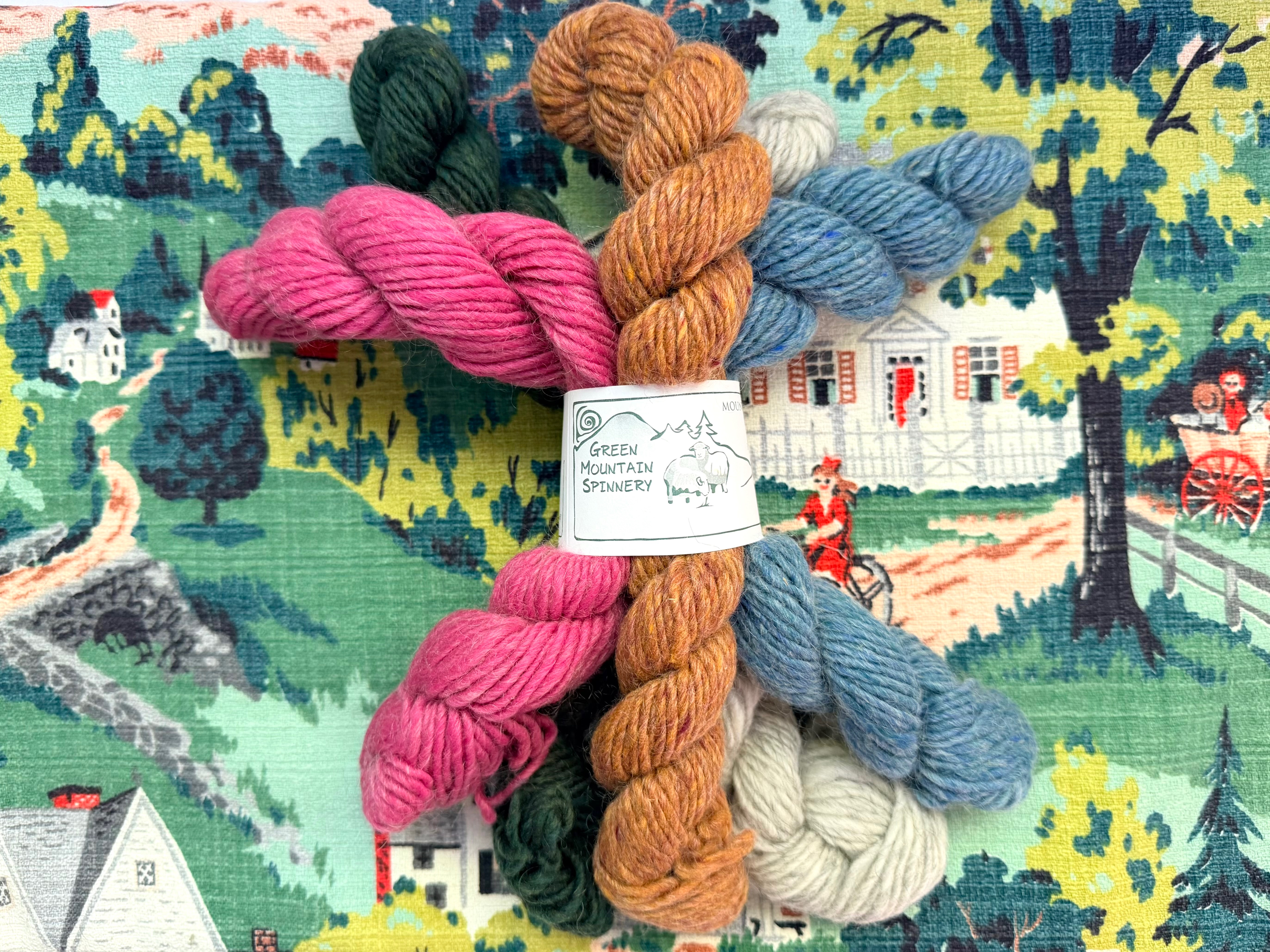 Storybook Yarn — illustrated still-life of skeins in front of a storybook cottage scene